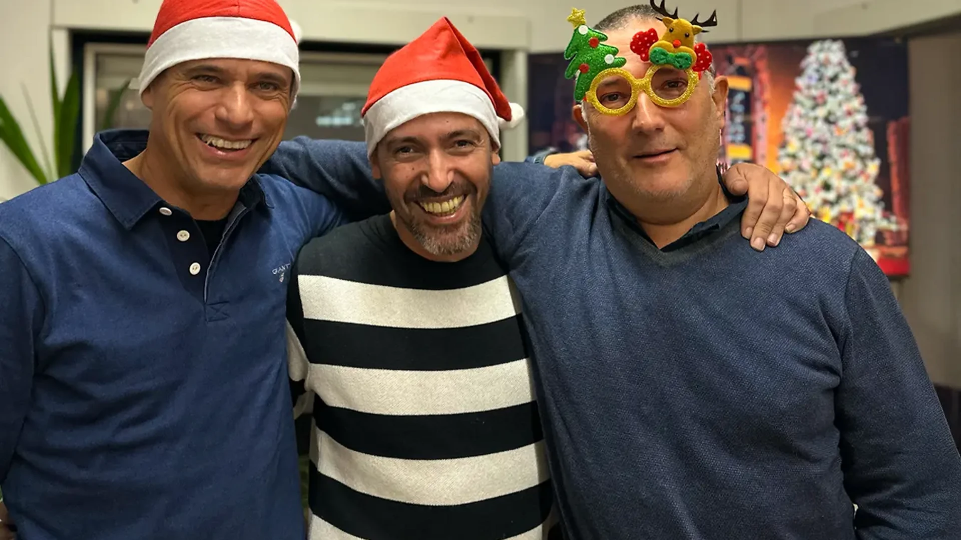 Founders wearing Santa hats and festive glasses pose closely together, smiling and hugging in front of a Christmas backdrop.