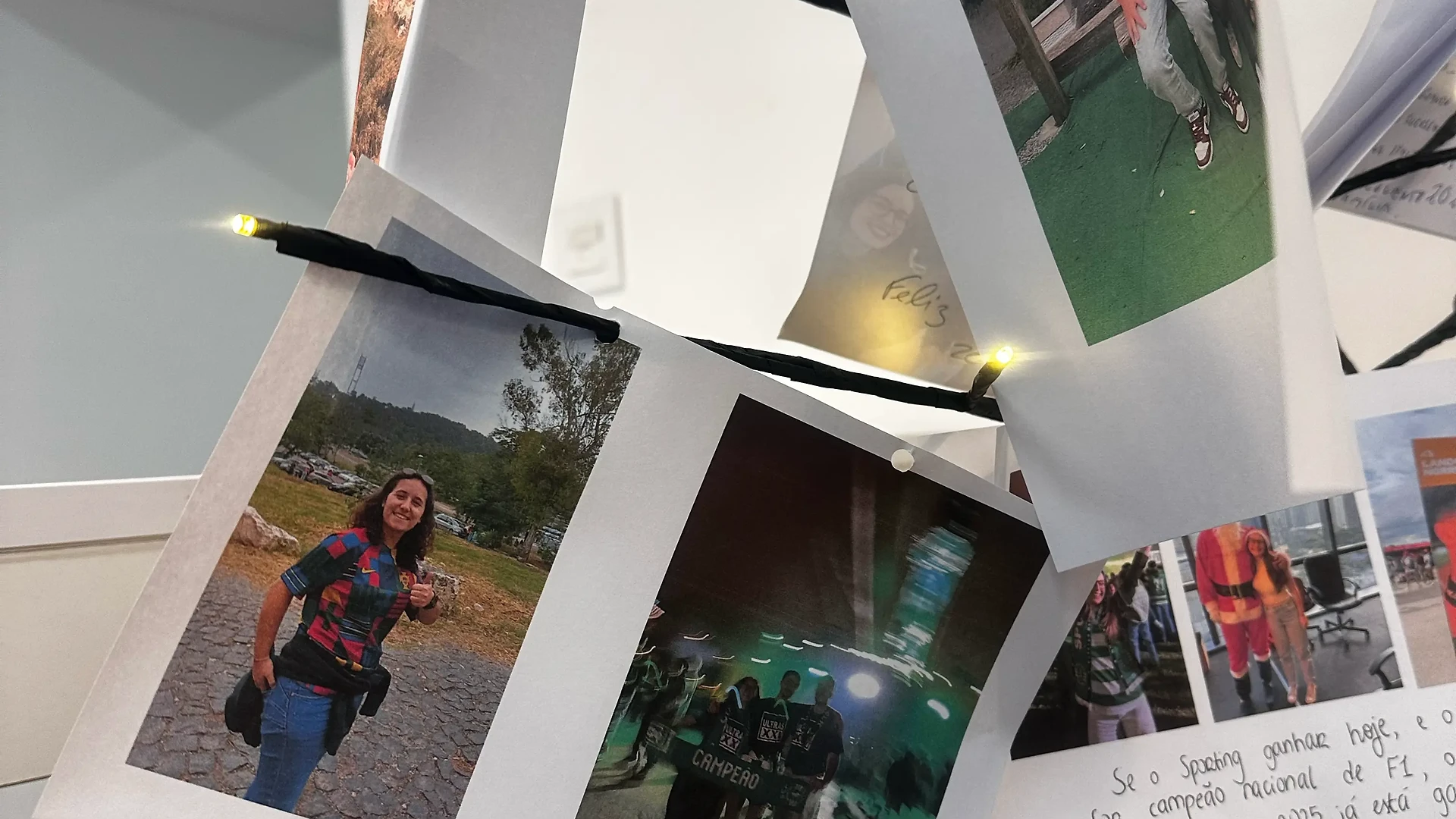 A small decorative Christmas tree with warm white lights, displaying printed team photos and holiday messages clipped to its branches.