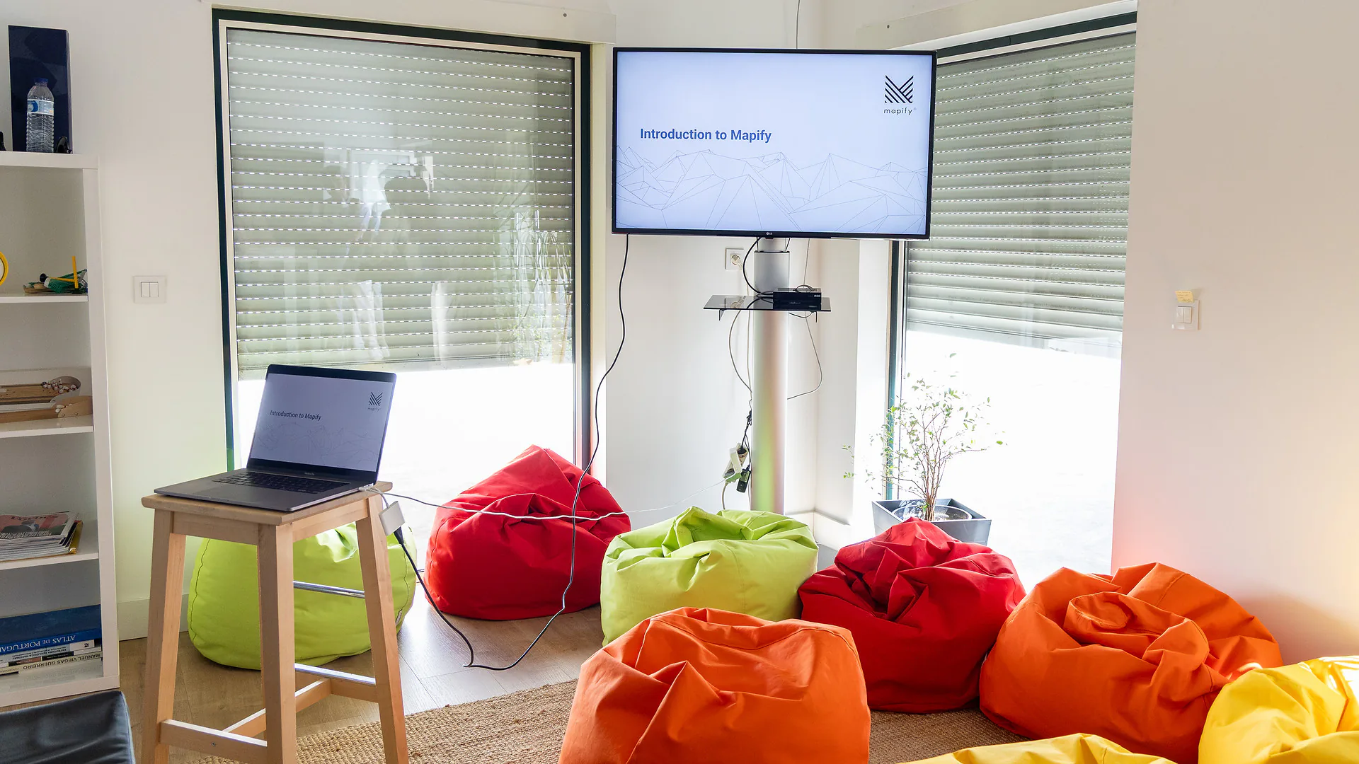 Over-the-shoulder view of a participant’s laptop screen displaying the Mapify website, with the tagline “Mapify for Education is our commitment to the future of geospatial analysis.” The colorful beanbags from earlier are visible in the background.