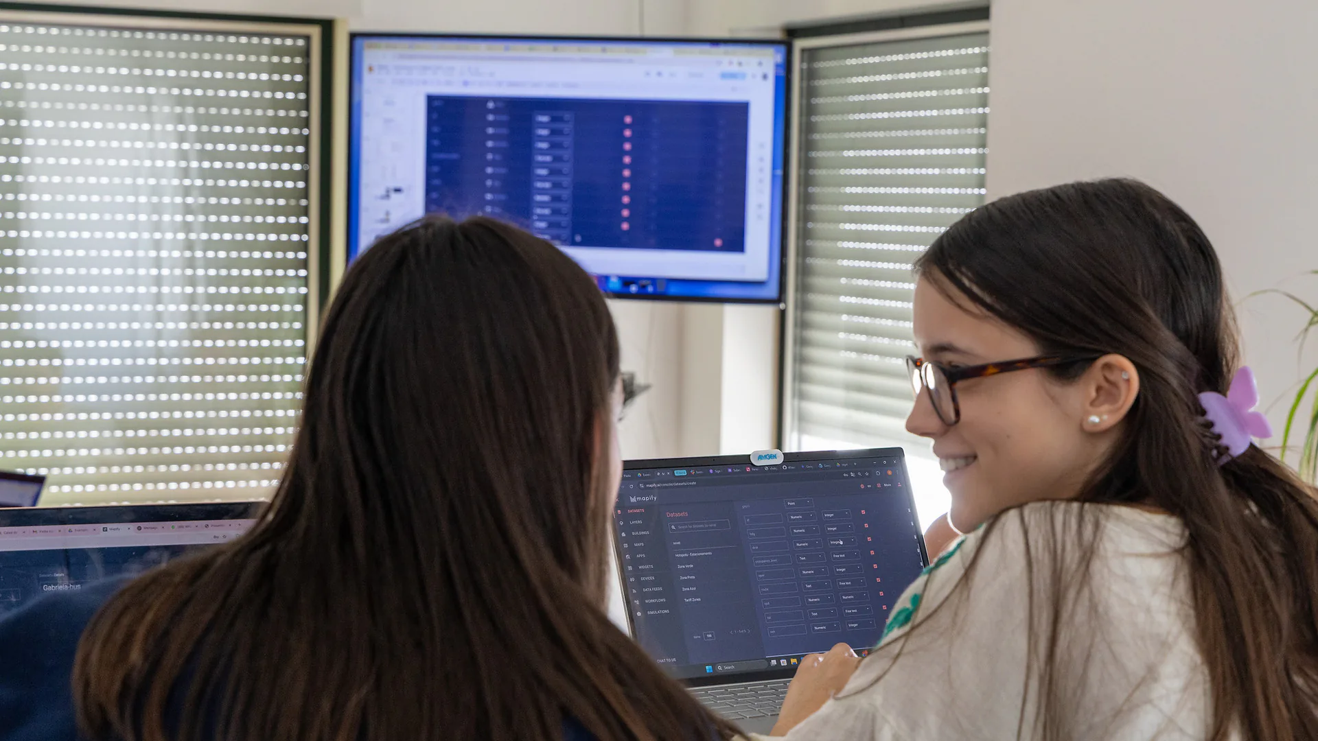 Mario Sobral stands in front of a group, gesturing with both hands as he leads a session. A poster behind him reads “Mapify – Create your IoT application without a single line of code.” The room is bright, with a laptop and books on a shelf.