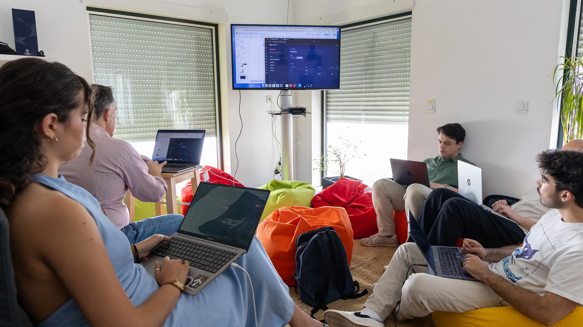 A wider view of the same session, showing Mario Sobral addressing a larger group of Junitec members in a modern kitchen area. Some participants stand, others lean on counters, listening as Mario gestures with his hand.