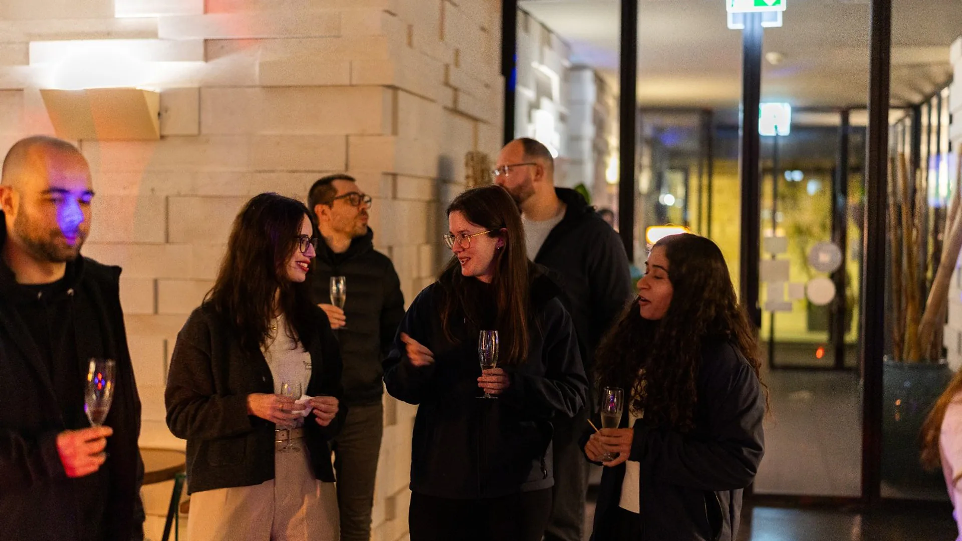 Presenter standing in front of a screen displaying slides, speaking to an audience seated at long tables.