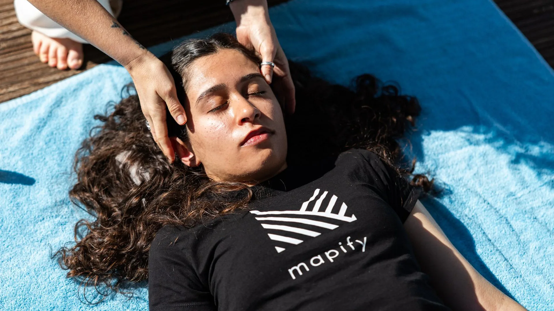 Man standing near a screen during a presentation, resting his hand near his face while listening.