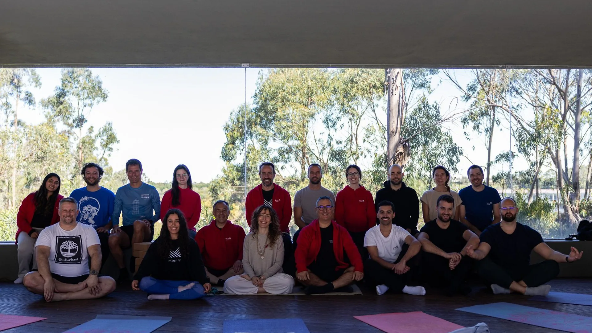 Group of colleagues standing indoors chatting and holding drinks during a karaoke night, with warm lighting and a relaxed atmosphere.