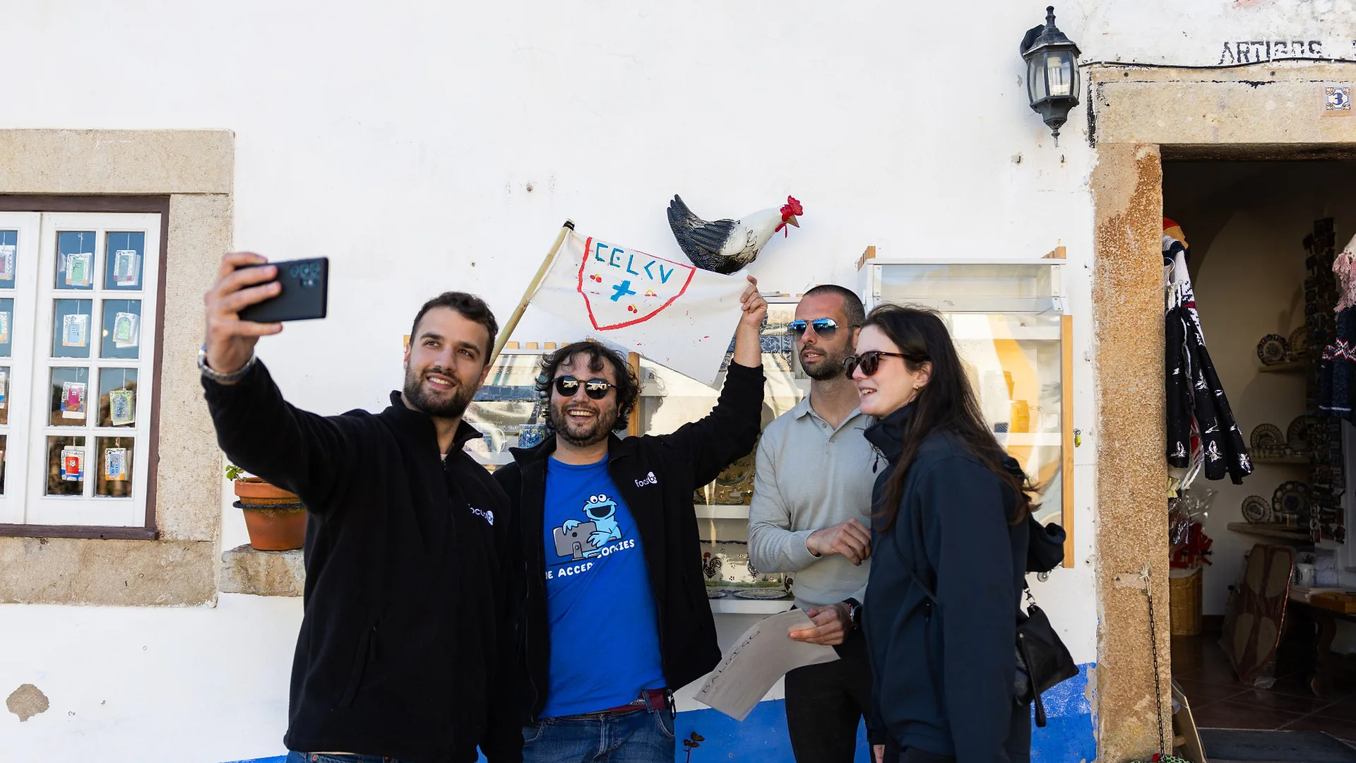 Two men looking down at a phone while others stand nearby, appearing to choose a song during karaoke night.