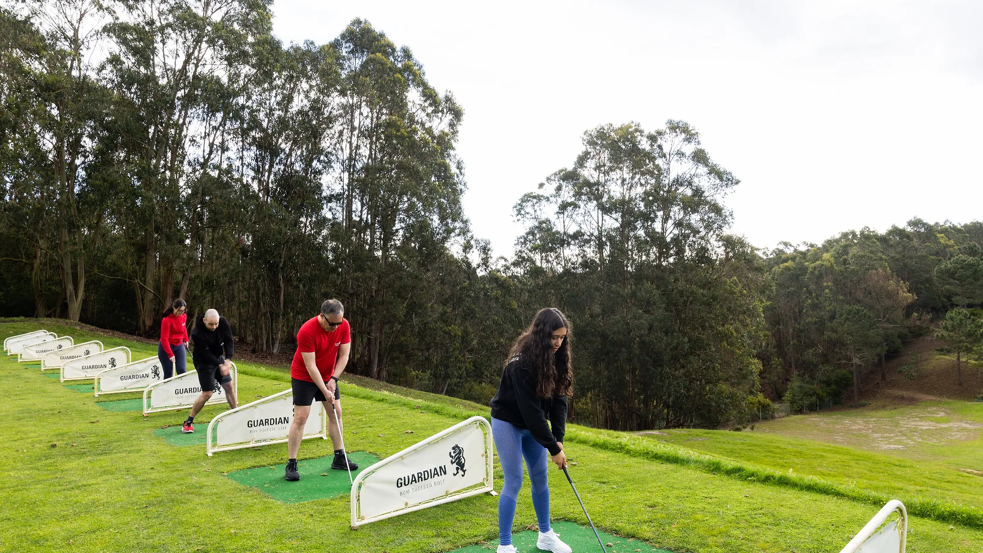 Man in a red jacket singing energetically into a microphone under colorful party lights, with colleagues watching during karaoke night.