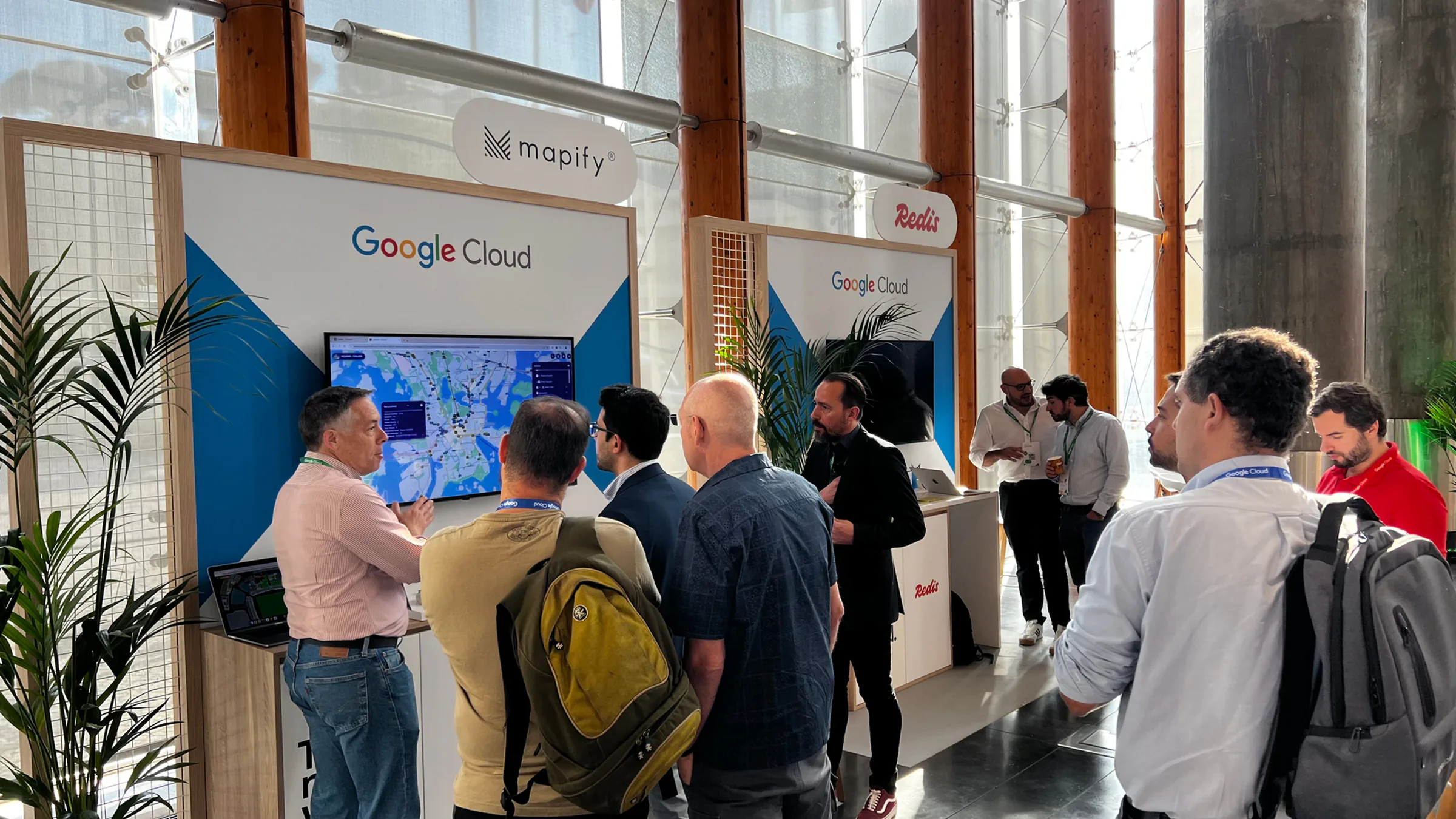 Attendees gathered at a Google Cloud and Mapify booth, watching a live demo on a large screen while speaking with representatives in a bright event hall.