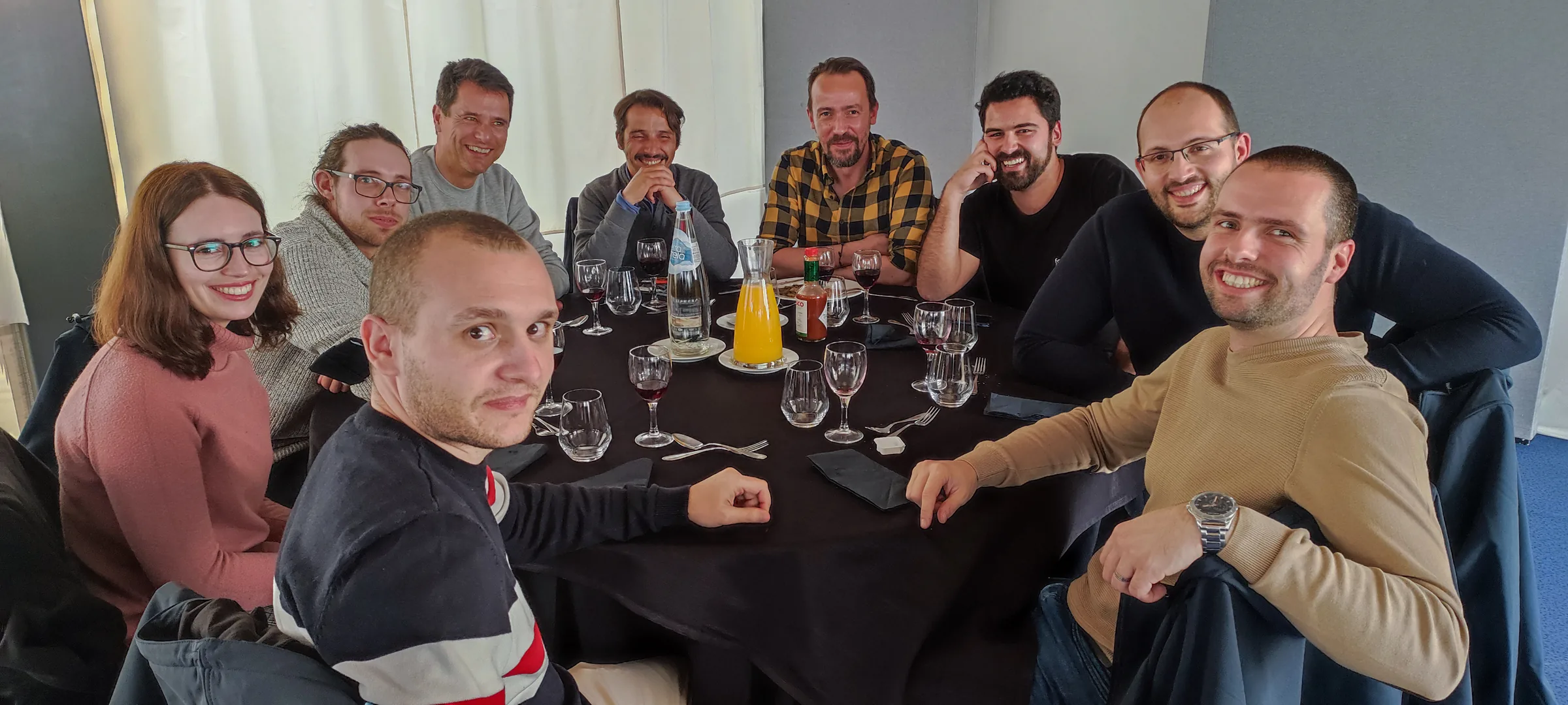 Group of colleagues smiling around a dining table with drinks and glasses, posing for a team lunch photo.