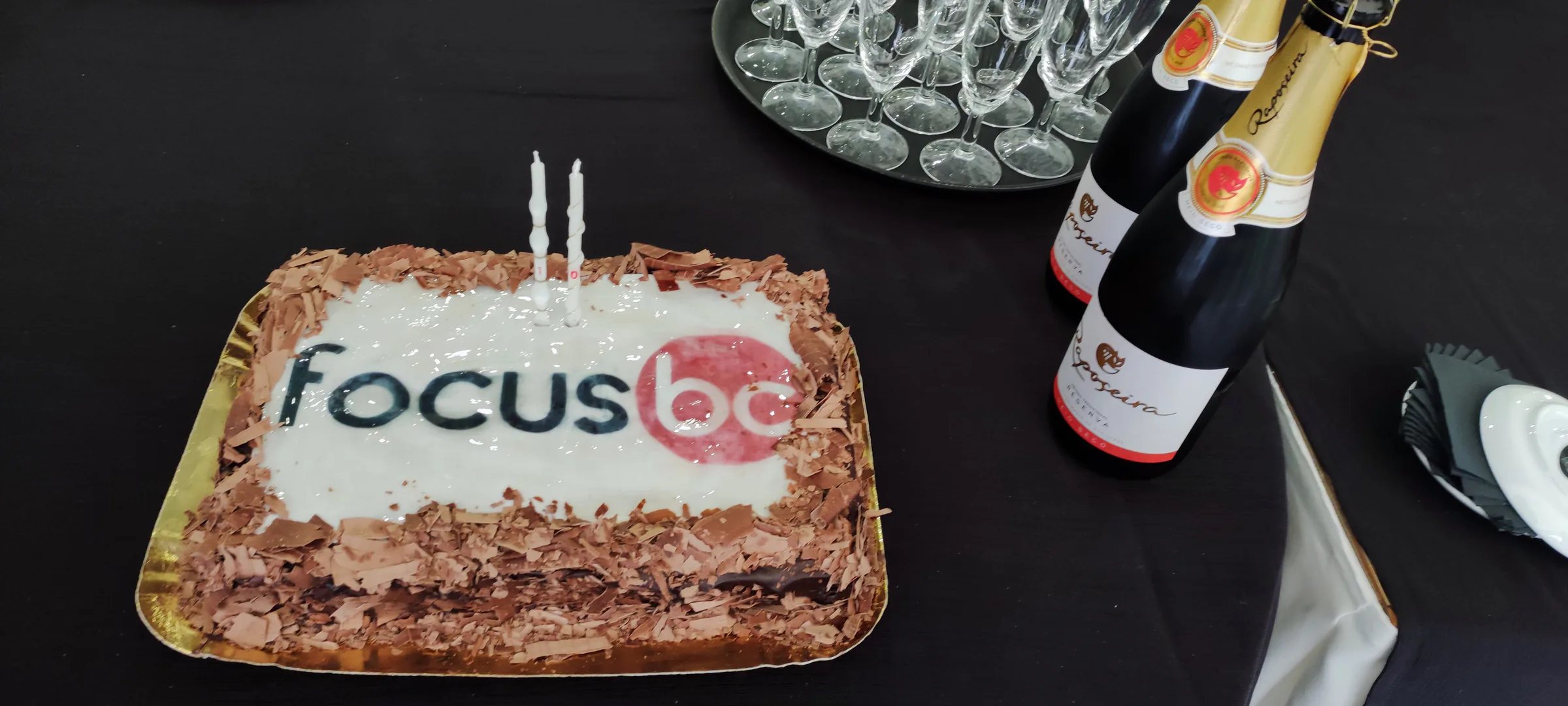 Celebration cake with the Focus BC logo next to bottles of sparkling wine and empty glasses on a table.